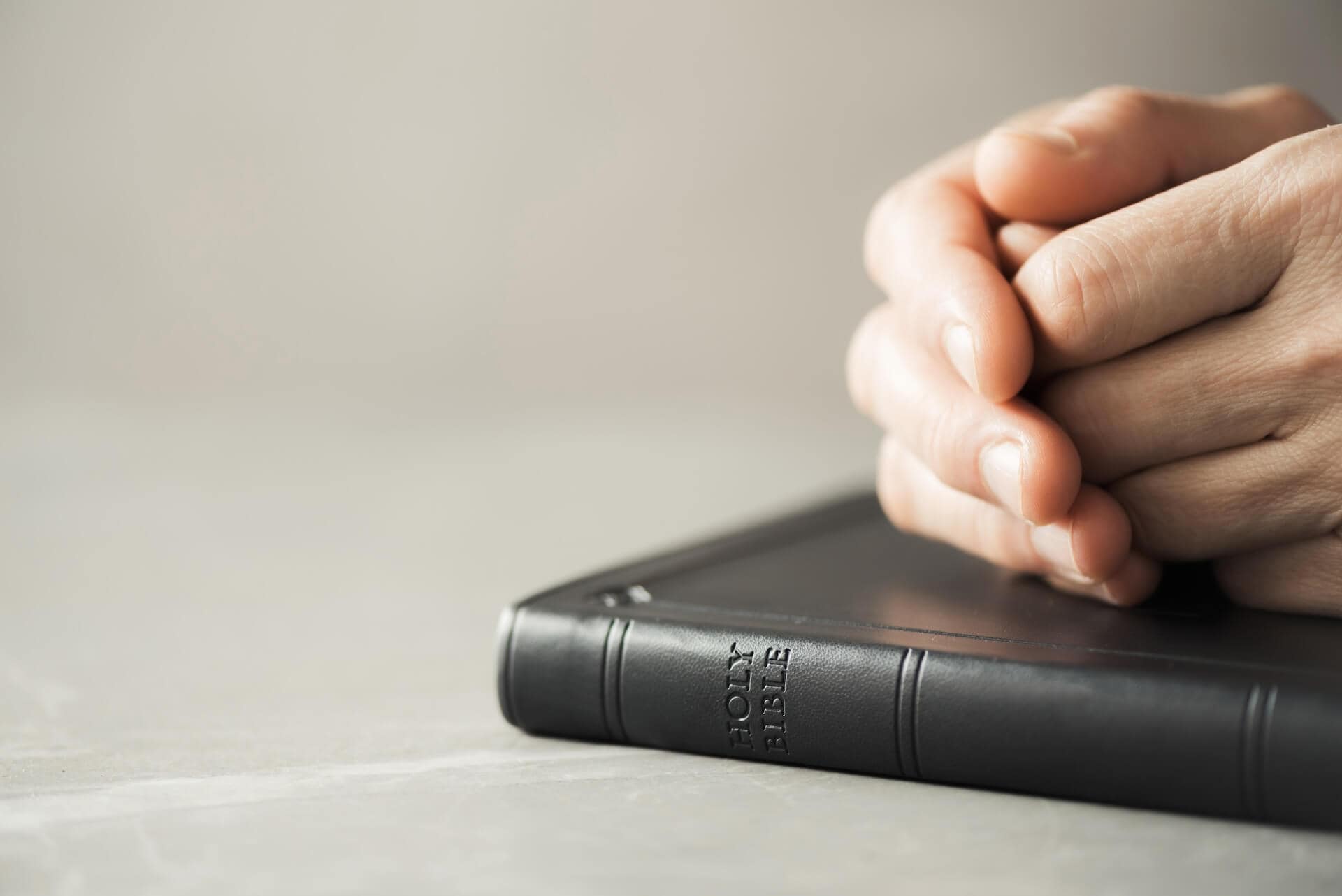 Hands closed in prayer on Bible